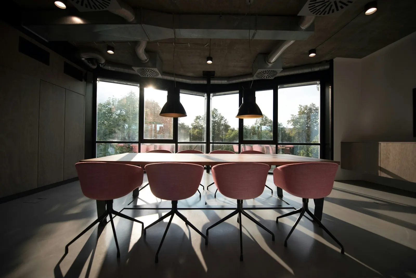 Sala de reuniões com mesa e cadeiras sob luminárias